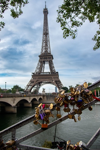 Paris, France – June 12, 2019: A vertical shot of love locks on railings, and the Eifel tower in the background in early morning, Paris France