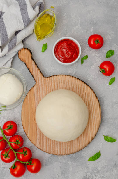 istock Fresh pizza dough with tomato sauce, mozzarella, tomatoes and basil leaves on a gray concrete background. Italian cuisine. Copy space. 1455923227