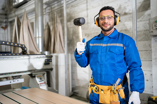 Portrait handsome carpenter in safety uniform holding hammer at wood factory
