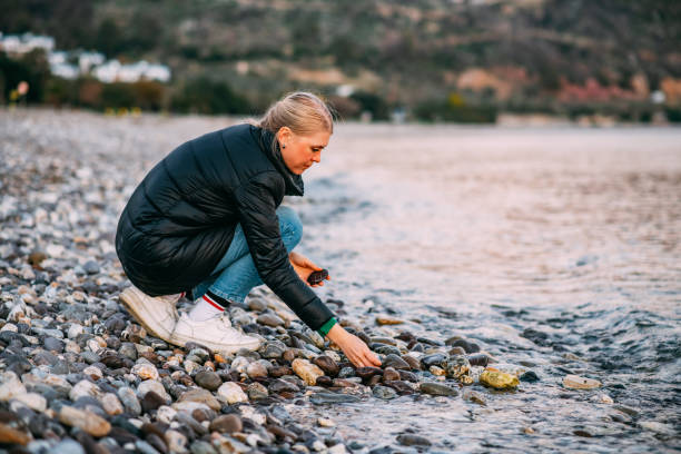 istock Young Woman Collects Pebbles on the Beach 1455923365