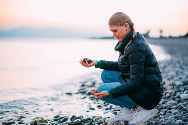 istock Young Woman Collects Pebbles on the Beach 1455923439