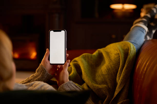 istock Woman At Home Lying On Sofa In Lounge With Cosy Fire Using Blank Screen Mobile Phone 1455926817