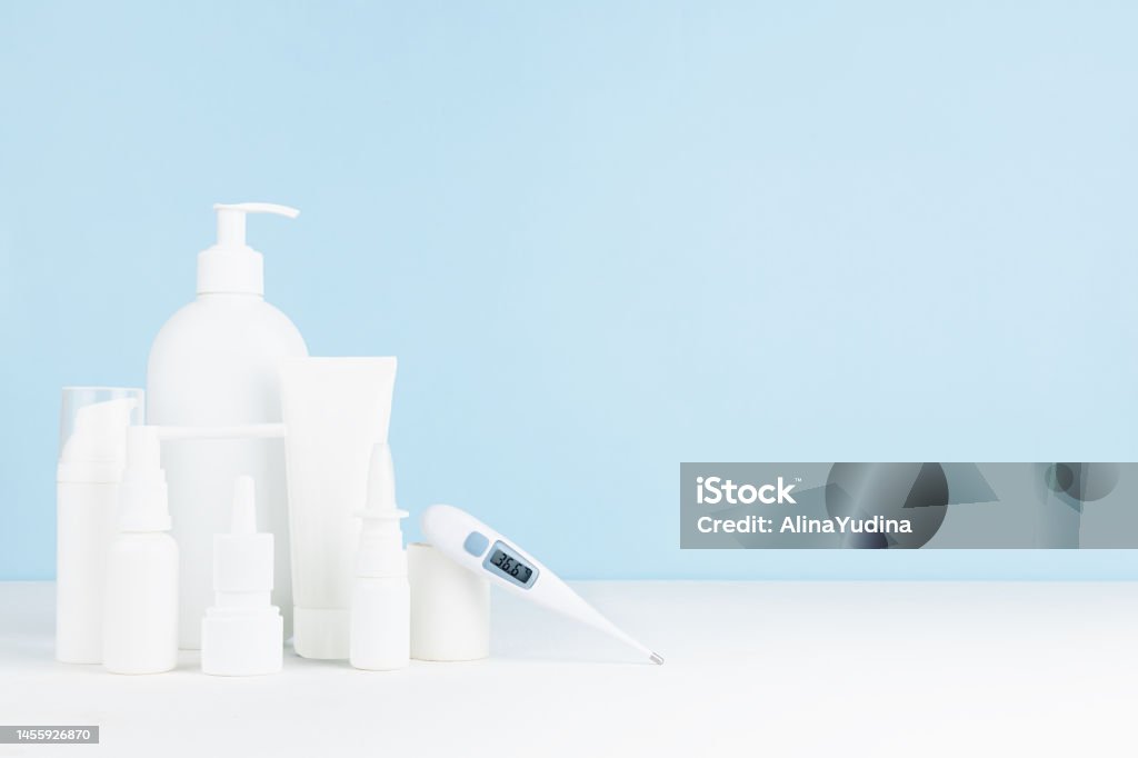 Medical and treatment background with white bottles mockup for prevent and teraphy disease and sickness, health and hygiene - 36,6 thermometer, sprays, salves on white table, blue wall, copy space. Advertisement Stock Photo