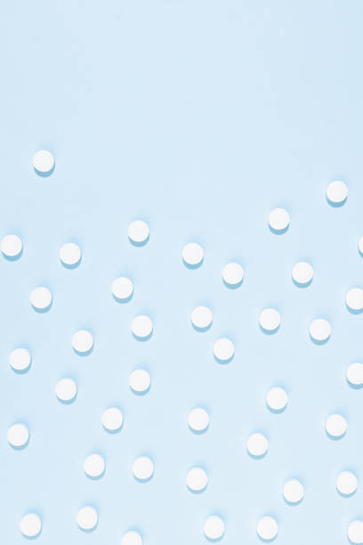 белые таблетки или таблетки выдерживают рисунок на мягком свете пастельно-голубого цвета при жестком освещении, вид сверху, вертикаль, гра� - vitamin pill vertical high key photographic effects стоковые фото и изображения