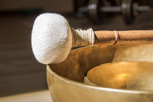 A closeup of two golden round singing bowls and a wooden struck on the table
