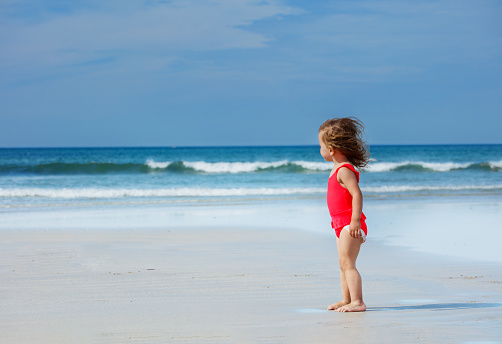 Cute little girl stand on beautiful ocean sand beach in swimsuit view in profile