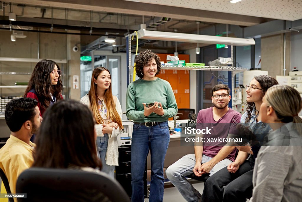 Technical college students exchanging ideas Relaxed group of Hispanic classmates smiling and talking in electrical engineering lab. Property release attached. Education Training Class Stock Photo