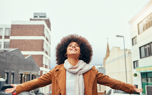 Black woman afro, freedom and love in the city for travel, tourism or vacation with smile in the outdoors. Happy African American female embracing free time, fresh air and adventure in the urban town