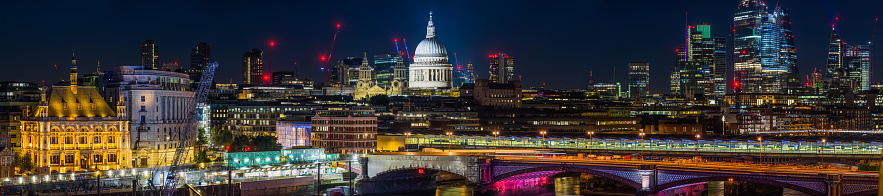 Aerial panoramic view across the River Thames to St. Paul’s Cathedral and the glittering skyscrapers of the City of London illuminated at night.