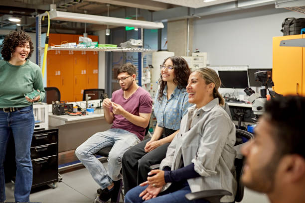 Laughing students enjoying electrical engineering class Age-diverse group of men and women sitting, smiling, and talking in university lab. Property release attached. job retraining stock pictures, royalty-free photos & images