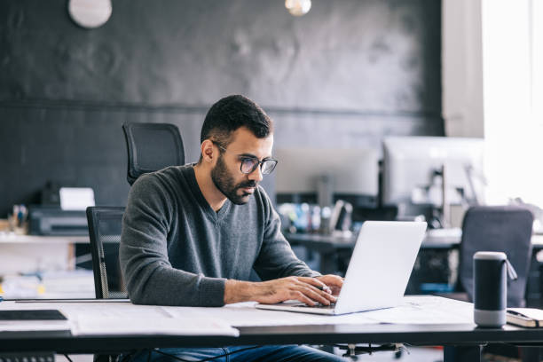 the architect takes notes on the blueprint, then inputs them into the laptop to keep an digital record of the design process. - men laptop businessman using laptop imagens e fotografias de stock