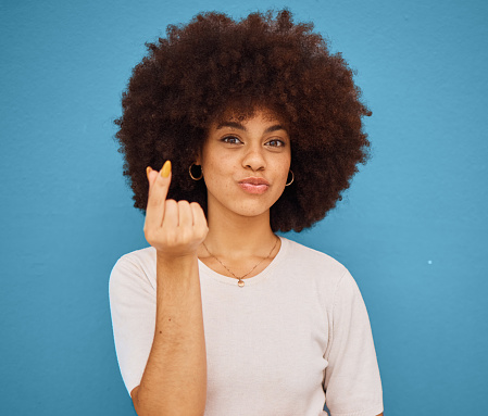 Hand, korean symbol and portrait of happy woman with an afro from Puerto Rico in the studio. Happiness, care and girl model doing kpop i love you gesture from Korea while isolated by blue background.