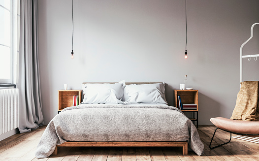 Retro-styled bedroom with a low hardwood bed and night tables with decoration (books, glasses, bottles), 2 simple pendant lights in the middle, an armchair, and a coat hanger on the hardwood floor in front of a white plaster wall with copy space.  A radiator heater under a retro window with gray curtains on one side. A slight cross-process was added. 3D rendered image.