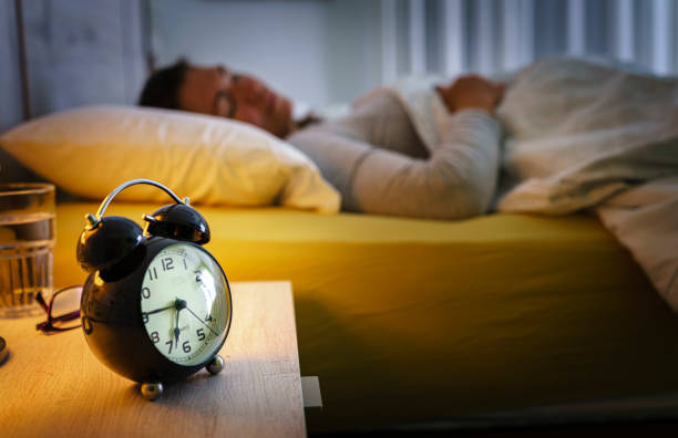istock Woman sleeping in bed at night with alarm clock on foreground 1455947684