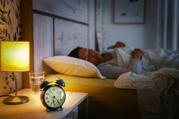 istock Woman sleeping on back in bed with alarm clock on foreground 1455947686