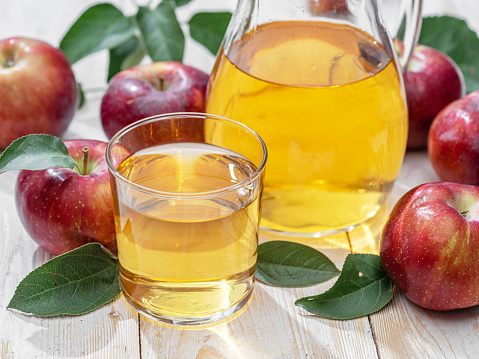 Glass of juice and carafe of fresh apple juice and organic apples on wooden table.