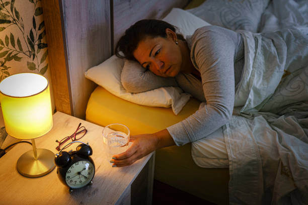 mulher sedenta alcança copo de água da mesa de cabeceira - sleeping insomnia alarm clock clock - fotografias e filmes do acervo
