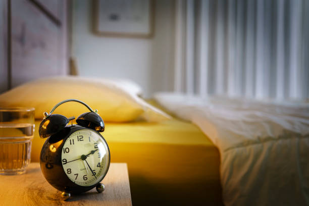 istock Alarm clock and waterglass on night table. Sleep disorder concept 1455947839