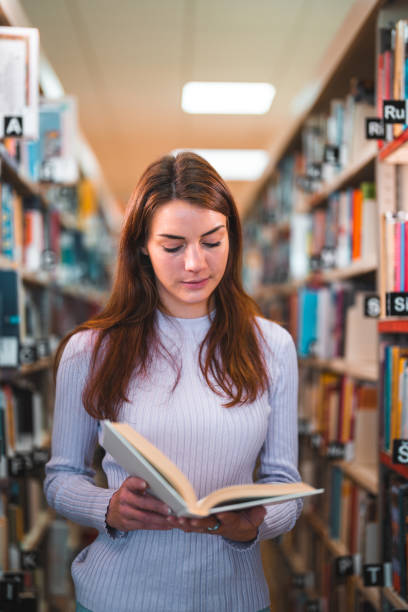 istock Caucasian Female Reading  A Book  Between Bookshelves In A Library 1455947902