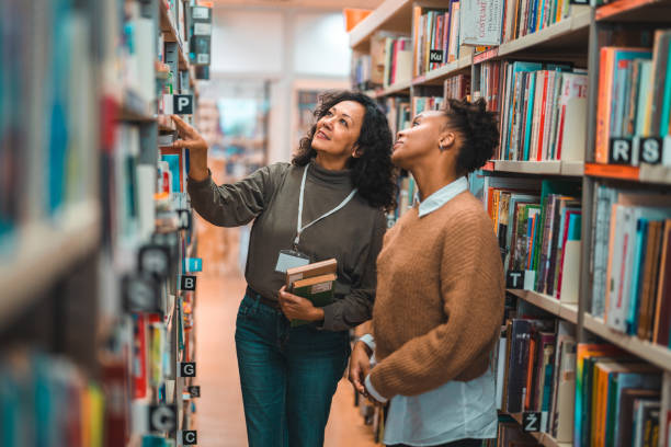 istock Mid Adult Hispanic Librarian Escorting A Student In A Library 1455947964