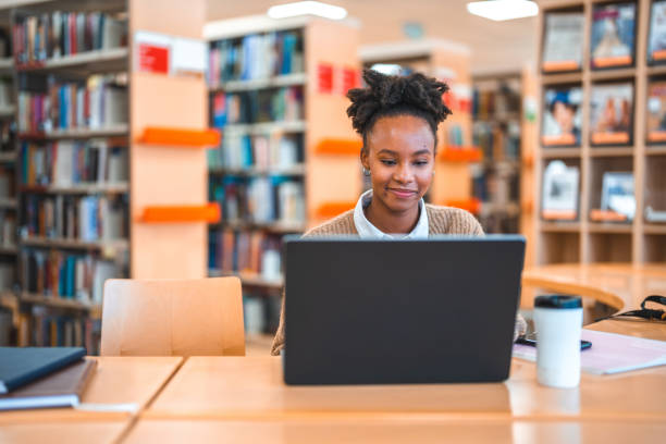 Estudante hispânica em 20s usando laptop em uma biblioteca - foto de acervo