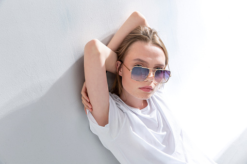 Blonde freckled girl wearing sunglasses. Photo studio with sunlight.