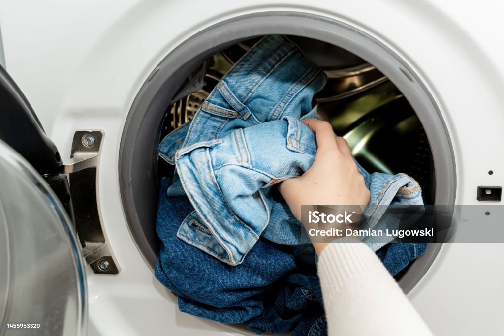 Person putting jeans into the drum of a washing machine, front view. Washing dirty jeans in the washer Washing Machine Stock Photo