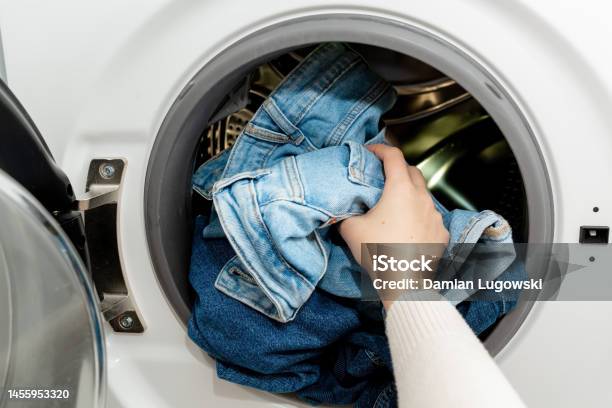 Person Putting Jeans Into The Drum Of A Washing Machine Front View Washing Dirty Jeans In The Washer Stock Photo - Download Image Now