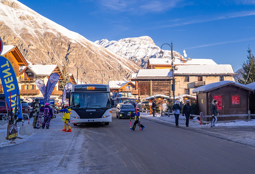 Livigno, Italy – January 12, 2022: The main shopping street surrounded by mountains - Via Plan with cars and a bus