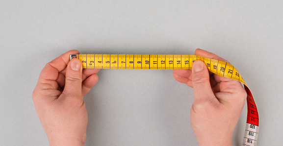 Hand holding yellow tape measure, fitness and diet concept, control with measurement