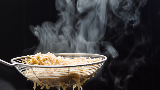 Noodles in a basket that just boiled from hot soup pot with steam selective focus,soft focus