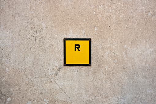 A closeup shot of a letter R in the yellow square on the old wall