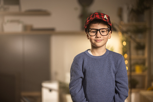 Portrait of a cute young boy with eyeglasses standing in living room at home.