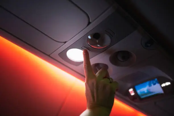 Photo of A woman adjusts the airflow and the brightness of a light bulb in an aircraft cabin