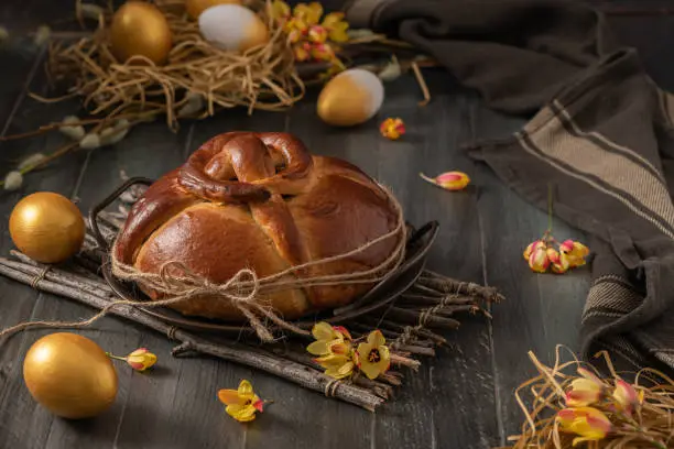 Photo of Portuguese traditional Easter cake. Folar with golden eggs on easter table. Blossom flowers and golden painted eggs.