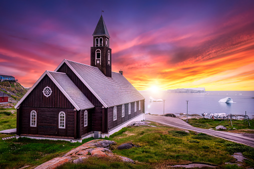 Midnigh sun sunset in the arctic with Zion´s church at Ilulissat with enormous icebergs floating in front