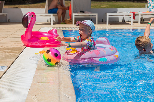 Young girl sitting in a floatation device in a swimming pool while on holiday in Benalmadena. She is reaching for a ball on the side of the pool.