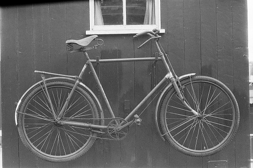 Black and white film photograph of an old rusted bicycle hanging on an external wall