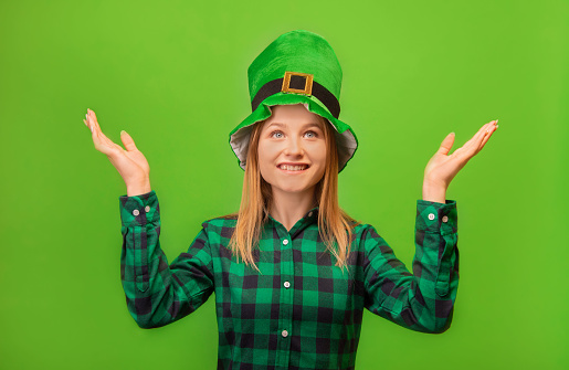 Happy smiling girl wearing green leprechaun hat with green checkered plaid shirt and raising hands up isolated on colorful green background.

Saint Patrick Day, sorry, don't know and can't say concept.