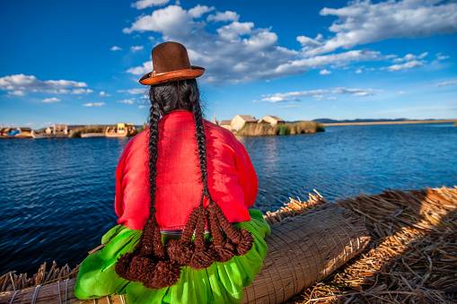 Peruvian woman admiring the view on Uros floating island, Lake Tititcaca. Uros are a pre-Incan people that live on forty-two self-fashioned floating island in Lake Titicaca Puno, Peru and Bolivia. They form three main groups: Uru-Chipayas, Uru-Muratos  and the Uru-Iruitos. The latter are still located on the Bolivian side of Lake Titicaca and Desaguadero River. The Uros use bundles of dried totora reeds to make reed boats (balsas mats), and to make the islands themselves. The Uros islands at 3810 meters above sea level are just five kilometers west from Puno port.