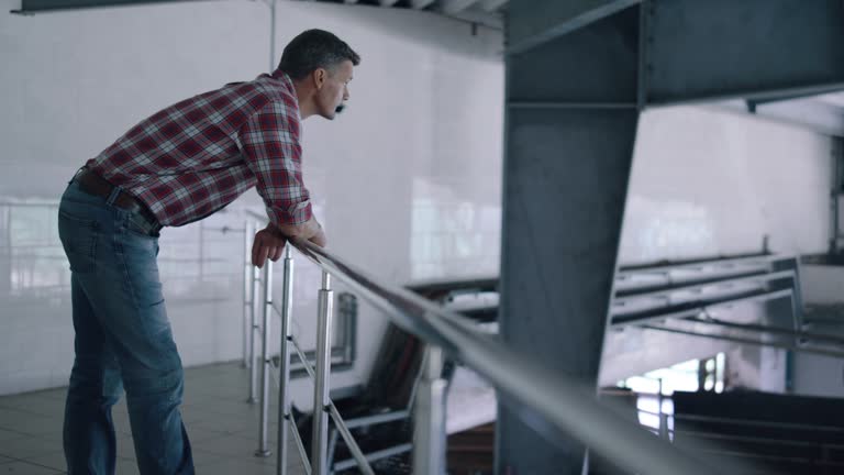 Worker watching milking facility leaning on railings. Agro engineer inspecting.