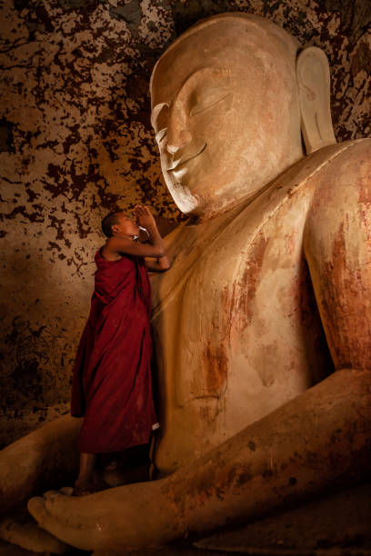 A small novice monk from Myanmar among red robes drying wet