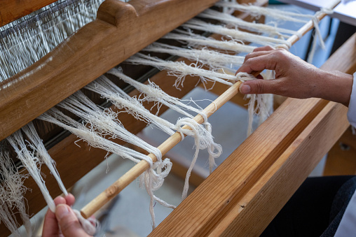 A traditional rug being woven on a carpet vertical loom, showing wool pile under tension, foundation, warp and weft . threads on a loom in close-up.