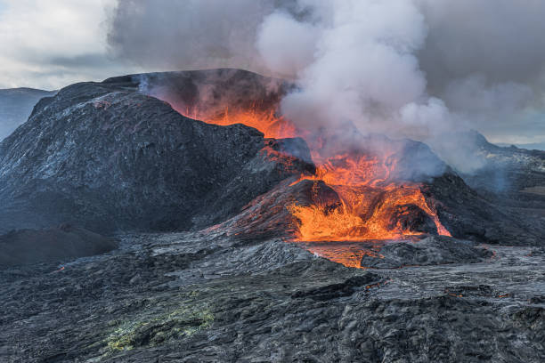 Volcano on Iceland after eruption. Hot steam clouds over crater opening. Lava flows from the volcanic crater. Landscape on Reykjanes peninsula at day. dark magma rock in the foreground