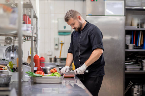 istock Professional chef in uniform cut fresh vegetables in kitchen. Cook man cooking delicious garnish for clients in restaurant. Culinary concept 1455975605
