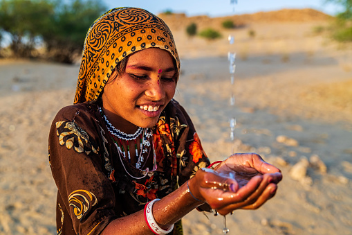 Indian little girl is drinking fresh water, desert village, Thar Desert, Rajasthan, India. Potable water is very precious on the desert - Rajasthani women and children often walk long distances through the desert to bring back jugs of water that they carry on their heads.