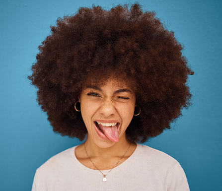 Face, portrait and woman with tongue out being silly and goofy on a blue studio background. Amusing, comic and crazy african american female making a funny, humour face on a backdrop