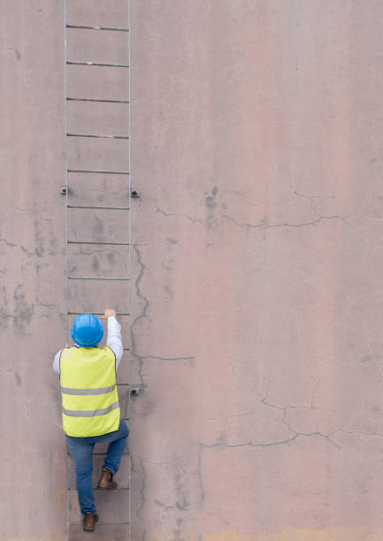 istock Engineer, building and man climbing ladder to get to roof or construction site. Engineering, safety and male maintenance, repair or installation contractor or worker going up steps on wall mock up. 1455979188