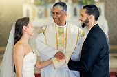 Wedding, priest and couple holding hands in church for a christian marriage oath and faithful commitment. Trust, bride and happy groom with a supportive pastor helping them make a holy love promise