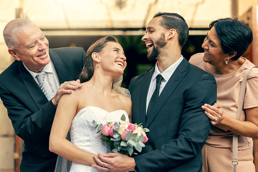 Wedding, happy and couple with parents at a celebration of love at an event with happiness. Smile, celebrate and young bride and groom after marriage with mother and father together at a church